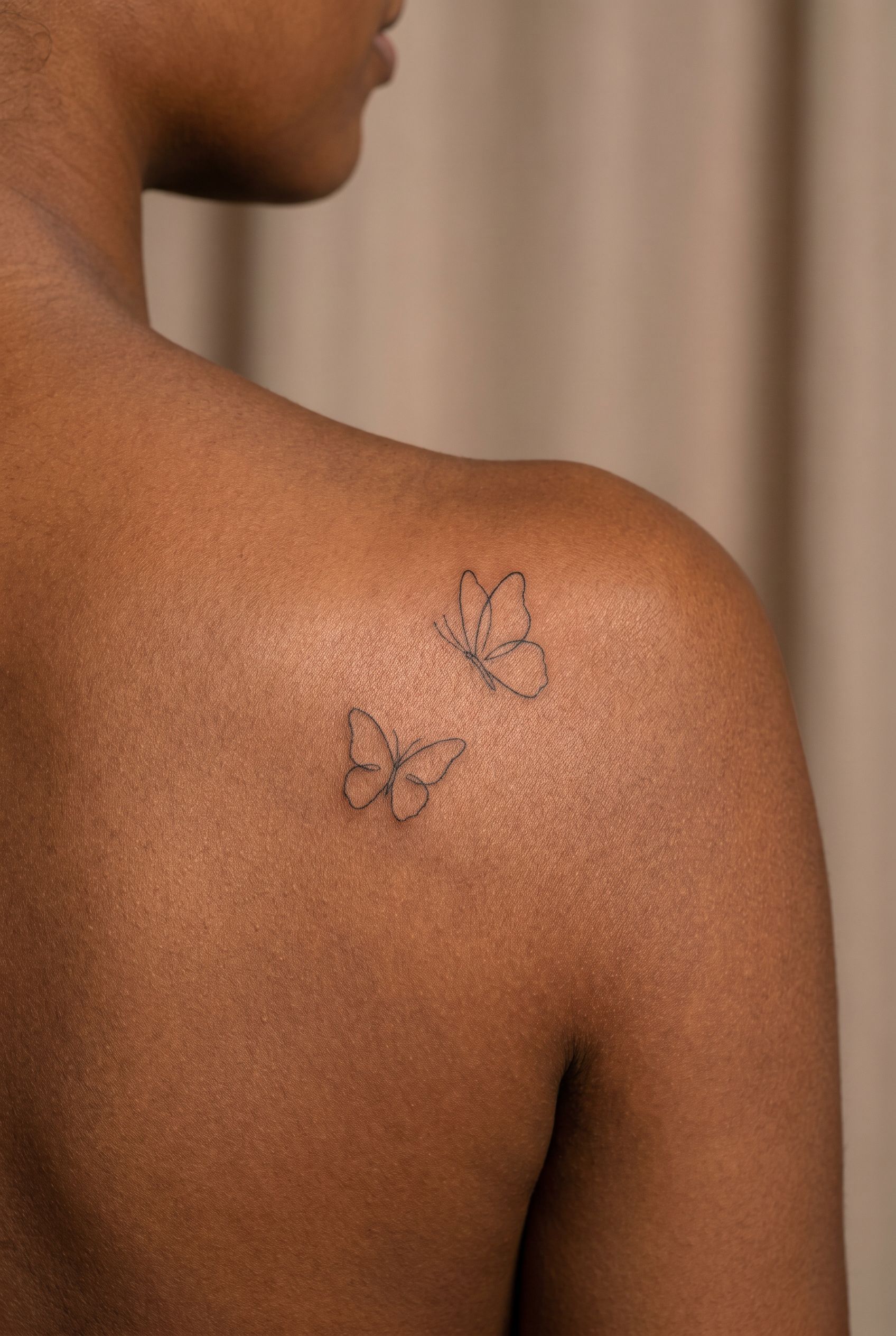 Deux papillons en fine line tatoués sur l'omoplate d'une femme